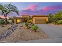 Charming tan home featuring desert landscaping and a three-car garage at sunset at 7152 E Night Glow Cir, Scottsdale, AZ 85266