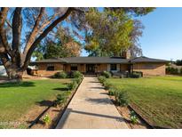 Charming brick home with mature trees, a stone pathway and lush landscaping at 547 W Orangewood Ave, Phoenix, AZ 85021