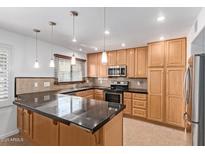An open kitchen with black countertops, wood cabinets, stainless steel appliances, and stylish pendant lighting at 4629 S Mill Ave, Tempe, AZ 85282