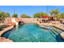 Stunning pool features a rock waterfall, slide, and a cozy dining area with an outdoor kitchen and seating at 11965 W Monte Vista Rd, Avondale, AZ 85392