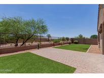 Backyard featuring a well maintained lawn, brick patio, and a metal fence. Tree provides shade, enhancing the outdoor experience at 41041 W Somers Dr, Maricopa, AZ 85138