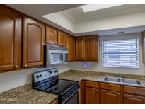 Well-lit kitchen features granite countertops, stainless steel appliances, and wood cabinets at 3330 W Danbury Dr # E203, Phoenix, AZ 85053