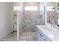 Modern bathroom with a glass-enclosed shower featuring stylish marble tile and a sleek, gray vanity with white countertop at 18047 W Long Lake Rd, Goodyear, AZ 85338