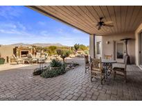 Charming covered patio featuring a stone fireplace, seating area, and desert landscaping with mountain views at 9802 E Hidden Valley Rd, Scottsdale, AZ 85262