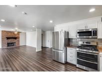 Open living room featuring modern stainless steel appliances, hardwood floors, and a charming brick fireplace at 1930 W Voltaire Ave, Phoenix, AZ 85029