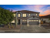 Striking two-story home showcasing a three-car garage, desert landscaping, and a tile roof against a colorful twilight sky at 11521 E Quintana Ave, Mesa, AZ 85212