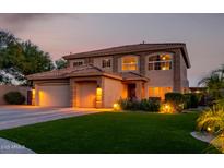 Inviting two-story home featuring lush green grass, a three car garage, and warm exterior lighting at twilight at 9569 W Redbird Rd, Peoria, AZ 85383