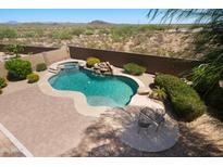 Inviting backyard oasis with a sparkling pool, waterfall feature, spa and desert landscaping in the background at 18375 E San Ignacio Ct, Gold Canyon, AZ 85118
