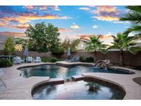 Inviting pool and spa with a rock waterfall feature, lounge chairs and umbrellas, surrounded by a block fence and palm trees at 2056 E Carob Dr, Chandler, AZ 85286
