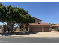 Inviting two-story home with a three-car garage, lush tree, and warm, earthy tones at 2213 N Ashbrook Cir, Mesa, AZ 85213