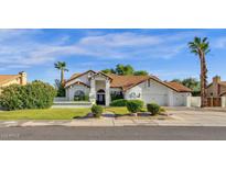 Beautiful single-story home with a tile roof, manicured lawn, mature trees, and a three-car garage at 9821 E Windrose Dr, Scottsdale, AZ 85260