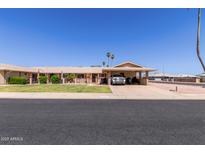 Charming single-story home featuring a covered parking, manicured lawn, and desert landscaping under a clear blue sky at 10439 W Kingswood Cir, Sun City, AZ 85351