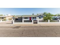 Charming single-story home with a gray exterior, red door, and a modern white brick and black horizontal slat fence at 325 E Harmony Ave, Mesa, AZ 85210