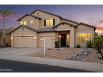 Inviting two-story home featuring a three-car garage, neutral stucco and desert landscaping at dusk at 18030 W Caribbean Ln, Surprise, AZ 85388
