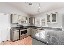 Well-lit kitchen with stainless steel appliances, grey cabinets, granite countertops, and terracotta tile floors at 3050 E Pontiac Dr, Phoenix, AZ 85050