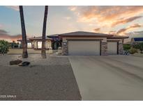 Charming home featuring a three-car garage, stone accents, and a meticulously landscaped front yard under a colorful sky at 15532 W Prairie Dunes Dr, Surprise, AZ 85374