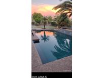 Backyard pool reflecting a colorful sunset with lush landscaping and palm trees at 15861 W Westview Dr, Goodyear, AZ 85395