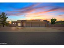 Inviting single-story home featuring a three-car garage and desert landscaping, bathed in the warm hues of a sunset sky at 4701 W Fallen Leaf Ln, Glendale, AZ 85310