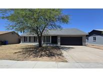 Charming single-story home featuring a well-maintained front yard with mature tree and a two-car garage at 8936 W Mackenzie Dr, Phoenix, AZ 85037