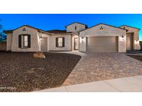 Home exterior showcasing a three-car garage, gravel landscaping, and a brick paver driveway at 18371 W Roma Ave, Goodyear, AZ 85395