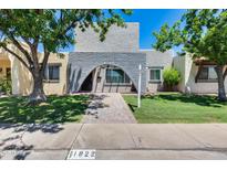 Two-story home with stone arched entrance, lush lawn, mature trees, and walkway to the front door at 1822 W Marlette Ave, Phoenix, AZ 85015