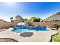 Backyard pool with small waterfall, umbrella, and desert landscaping at 13020 W Highland Ave, Litchfield Park, AZ 85340