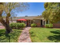 Charming home featuring lush green lawn, red brick walkway, and inviting front porch with red umbrella and door at 4710 N 33Rd Pl, Phoenix, AZ 85018