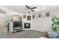 Cozy living room features neutral carpet, a corner fireplace, ceiling fan, and decorative Gathering artwork at 1374 E 10Th Pl, Casa Grande, AZ 85122