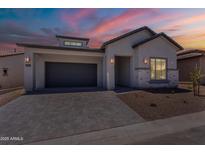 Beautiful single-story home featuring stucco and stone exterior and a paved driveway under a colorful sunset sky at 21427 W Meadowbrook Ave, Buckeye, AZ 85396
