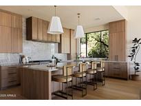 Modern kitchen featuring wood cabinetry, marble countertops, a large island, and pendant lighting fixtures at 12887 N 135 St, Scottsdale, AZ 85259