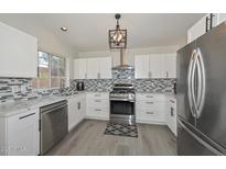 Modern kitchen boasts stainless steel appliances, granite countertops, stylish mosaic backsplash, and ample white cabinetry at 11224 W Puget Ave, Peoria, AZ 85345