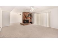 Spacious living room boasts a cozy brick fireplace, ceiling fan, and sliding glass door with bright, neutral carpet at 8501 E Malcomb Dr, Scottsdale, AZ 85250