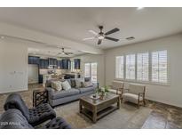 Comfortable living room with a grey sofa, ceiling fan, kitchen access, and bright natural light at 40759 W Bravo Dr, Maricopa, AZ 85138