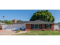 Charming brick home with a well-maintained lawn, a black roof, a brick chimney and a cozy front entrance with chairs at 1909 E Bethany Home Rd, Phoenix, AZ 85016