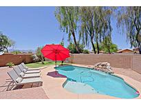 Beautiful backyard pool with waterfall feature, red umbrella, and lounge chairs perfect for relaxing at 42812 W Venture Rd, Maricopa, AZ 85138
