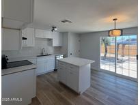 A bright kitchen features a kitchen island, wood flooring, white cabinets and stainless steel appliances at 5951 W Granada Rd, Phoenix, AZ 85035