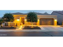 Inviting home exterior featuring warm lighting, a well-manicured lawn, and an attached two-car garage at dusk at 1673 E Laddoos Ave, Queen Creek, AZ 85140