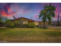 Charming single-story home featuring manicured lawn and mature shade tree under a colorful sky at 3936 E Oak St, Phoenix, AZ 85006
