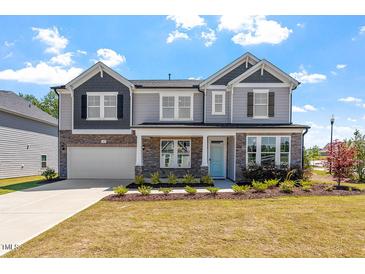 Beautiful two-story home with stone accents, a covered front porch, attached garage, and manicured lawn at 541 Henham Way, Zebulon, NC 27597