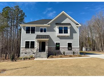 Two-story home with light gray siding, stone accents, black trim, and a manicured lawn on a sunny day at 168 Grand Griffon Way, Lillington, NC 27546