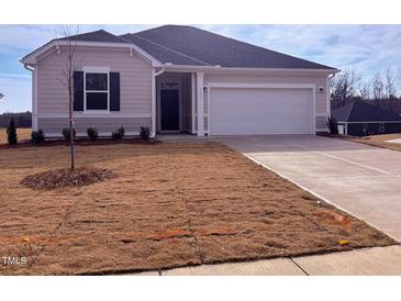 Beige house with a white garage door and landscaping at 1111 Woody Dr, Graham, NC 27253