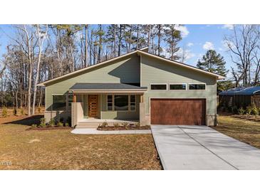 Modern house with green siding, brown garage door, and a landscaped yard at 5300 Pulley Town Rd, Zebulon, NC 27597