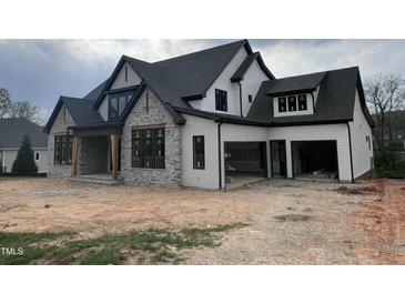 A modern farmhouse with stone accents, black trim, white siding, and a two-car garage under construction at 126 Harvest Ln, Pittsboro, NC 27312
