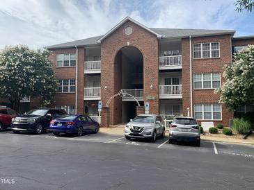 Red brick three-story condo building with arched entrance and white balcony railings in a landscaped parking lot at 129 Sturbridge Dr # 15, Clayton, NC 27520
