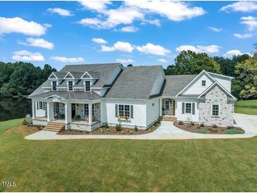 Beautiful white home with stone accents, a welcoming porch, and lush green lawn and a scenic lake view at 1618 Ben Wilson Rd, Mebane, NC 27302