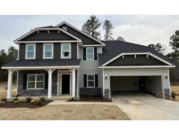 Charming two-story home with gray siding, stone accents, inviting covered porch, and an attached two-car garage at 19 Streamline Ct, Lillington, NC 27546
