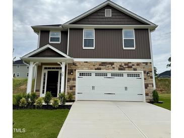 Two-story home featuring stone accents, brown siding, a two-car garage, and manicured landscaping at 320 Bishop Ln, Sanford, NC 27330