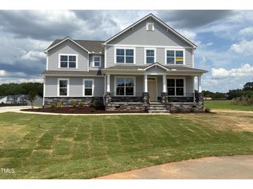 Beautiful two-story home featuring stone accents, a welcoming front porch, and lush green lawn at 111 Demascus Way # 021, Four Oaks, NC 27524