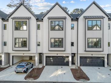Modern townhome featuring a stylish white exterior with black accents, garages, and manicured landscaping at 811 Maple Berry Ln # 103, Raleigh, NC 27607