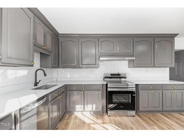 This kitchen features stainless steel appliances, gray cabinets, light countertops, and hardwood floors at 234 Crumpler Rd, Kenly, NC 27542